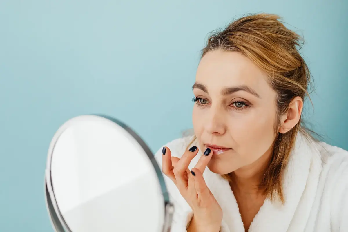 Femme qui applique un baume sur ses lèvres devant un miroir