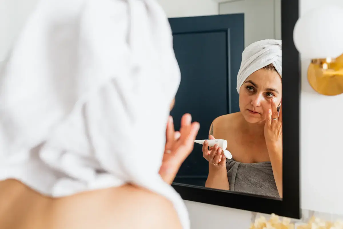 Femme qui applique un soin devant le miroir, une serviette sur les cheveux